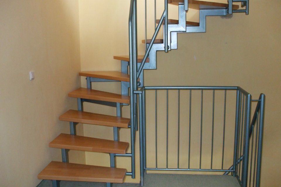 Treppe aus Metall und Holz mit Geländer vor einer hellbraunen Wand.