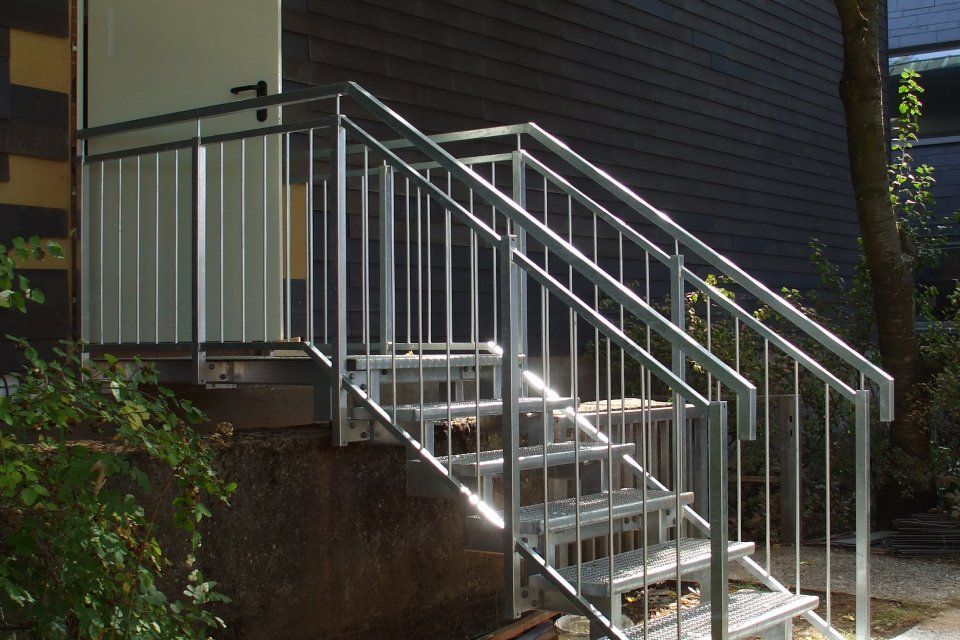 Metalltreppe mit Geländer, die zu einem Gebäudeeingang führt.