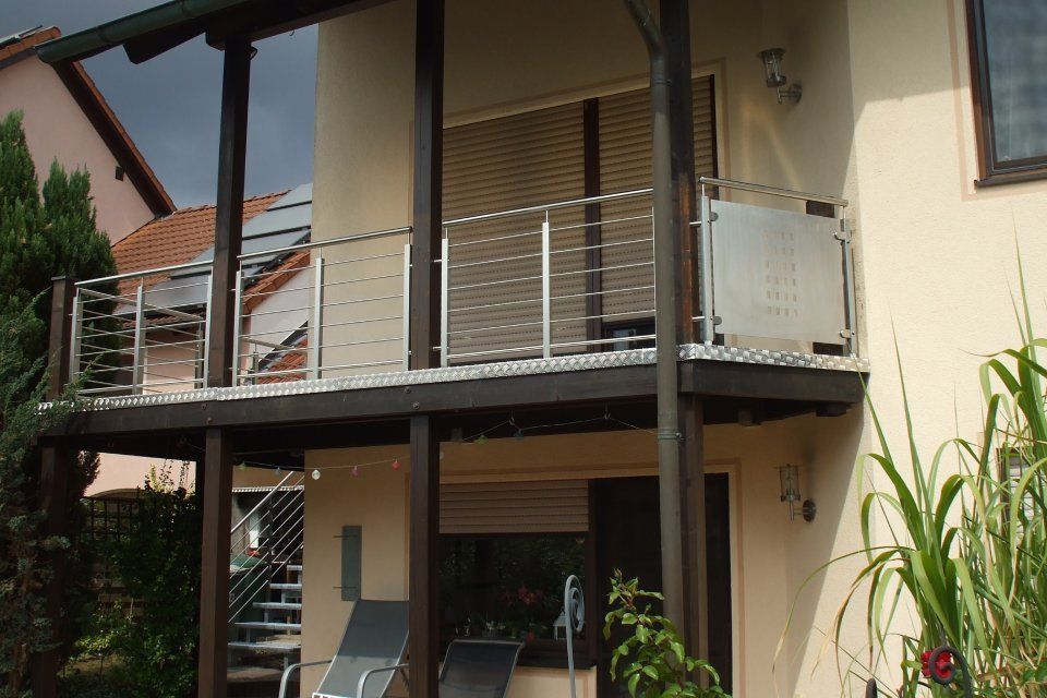 Balkon mit Edelstahlgeländer und Holzpfosten, mit Blick auf einen begrünten Hinterhof.