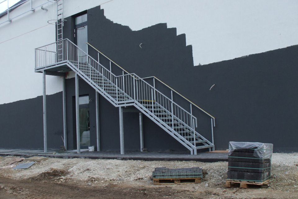 Eine Außentreppe aus Metall führt zu einer Tür an einem Gebäude mit grau-weißen Wänden.