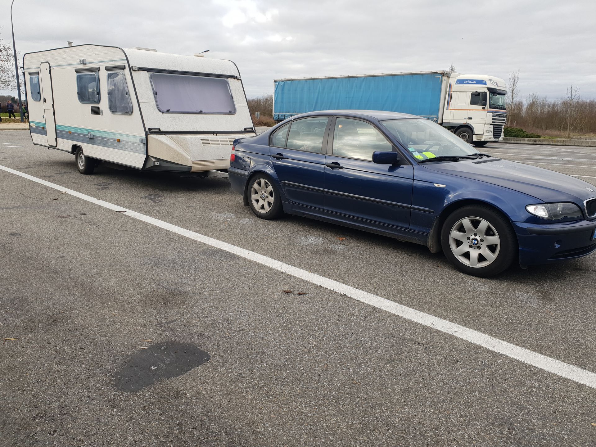 Une berline bleue tractant une caravane blanche sur le bas-côté d'une autoroute sous un ciel couvert.