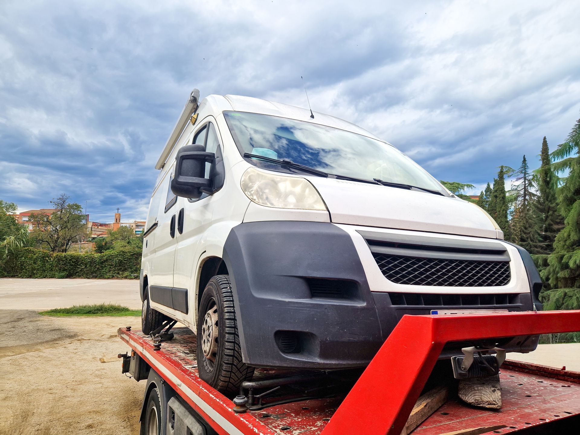 Un camping-car blanc sur une dépanneuse rouge à plateau sous un ciel nuageux.