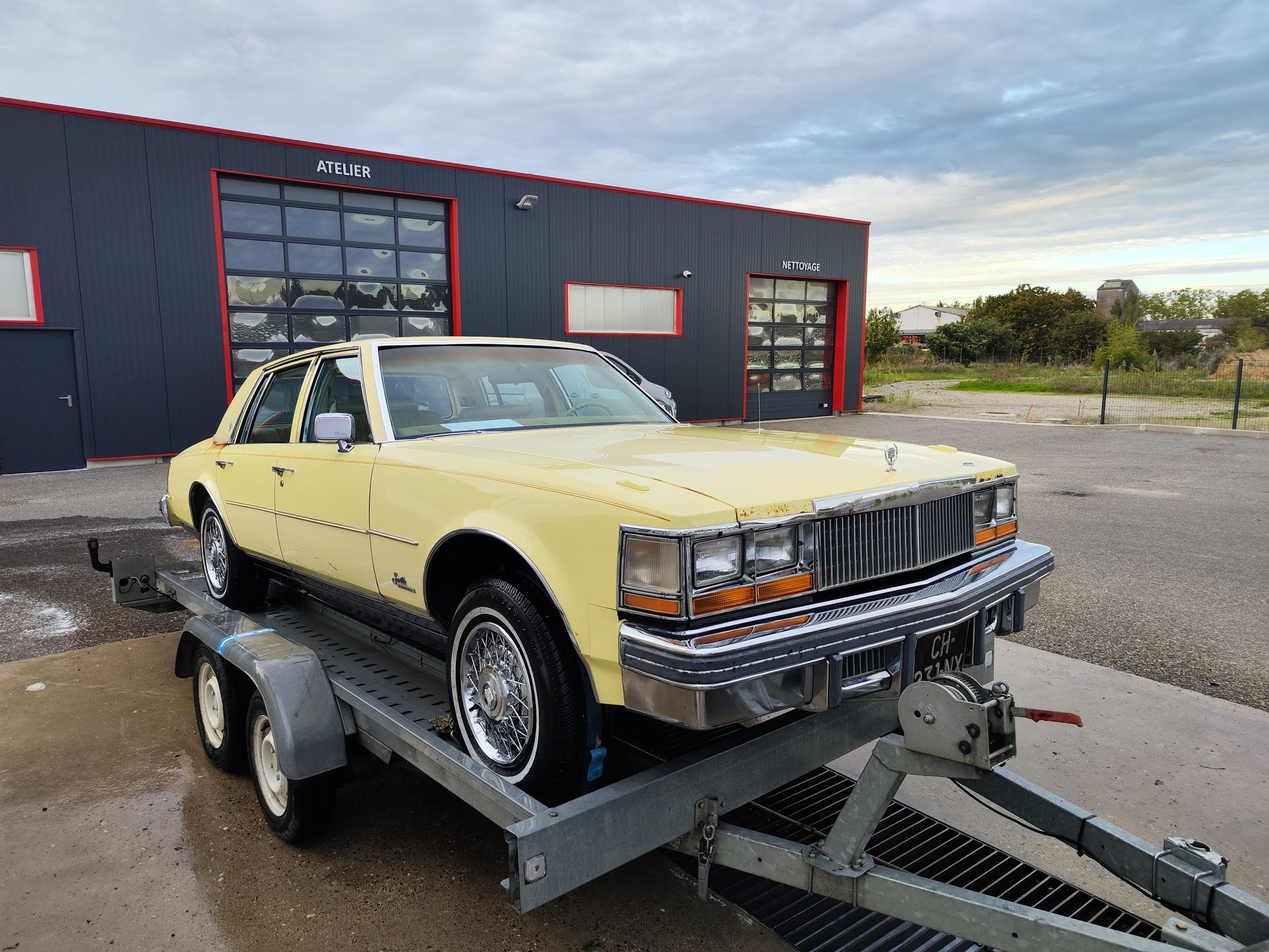 Une Cadillac Séville jaune sur une remorque près d'un garage.