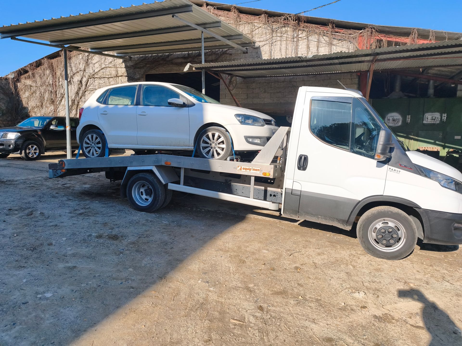 Voiture blanche chargée sur une dépanneuse dans un parking industriel ensoleillé.