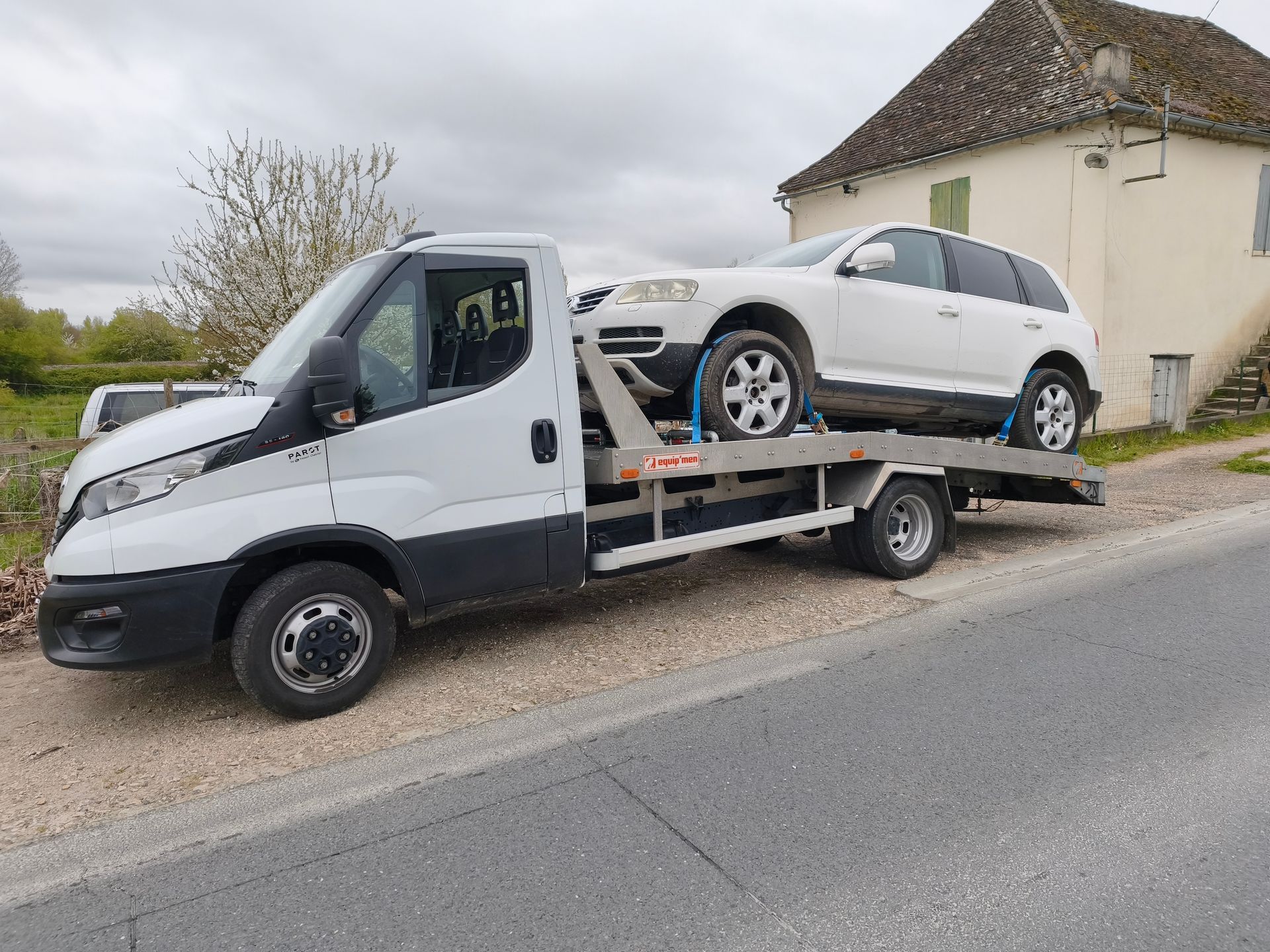 Une dépanneuse transportant une voiture blanche garée au bord d'une route près d'une maison.
