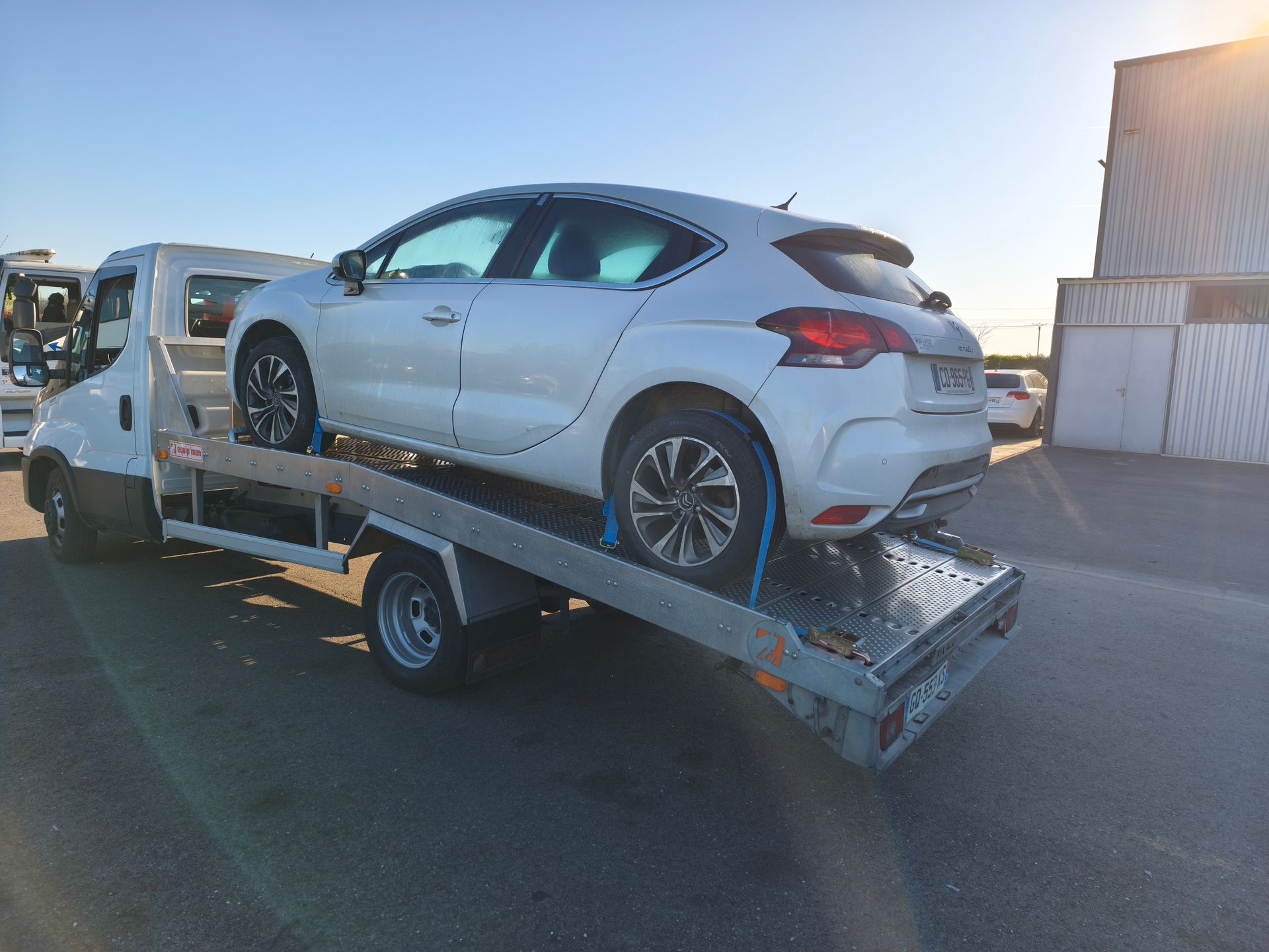 Voiture sur une rampe de remorquage dans une zone industrielle au coucher du soleil.