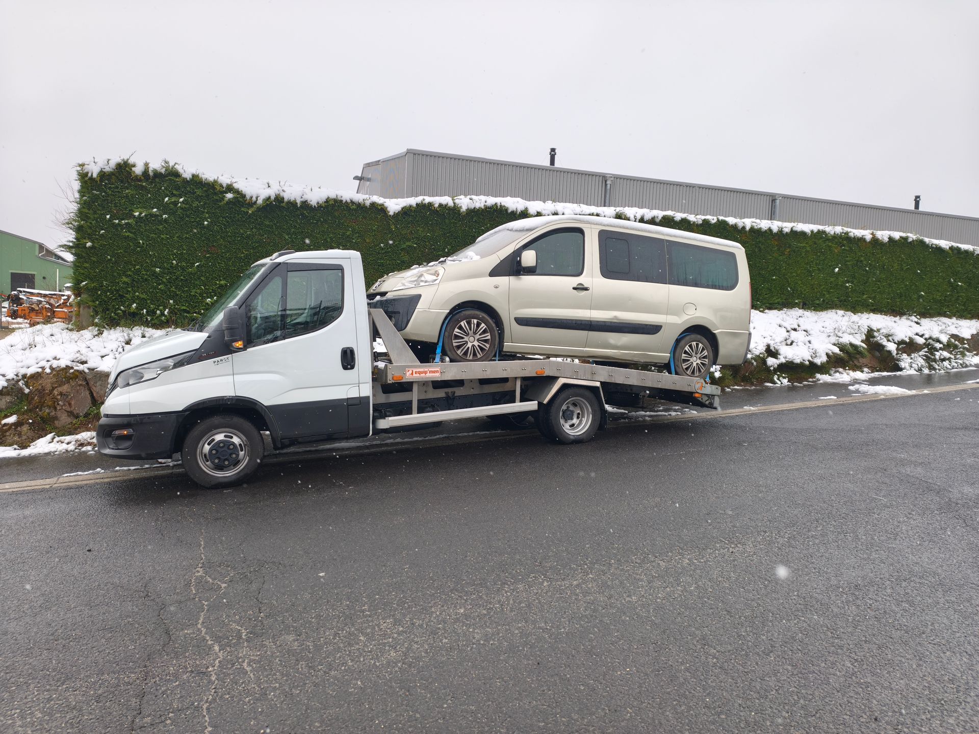 Une camionnette blanche chargée sur une dépanneuse à plateau au bord de route enneigée.