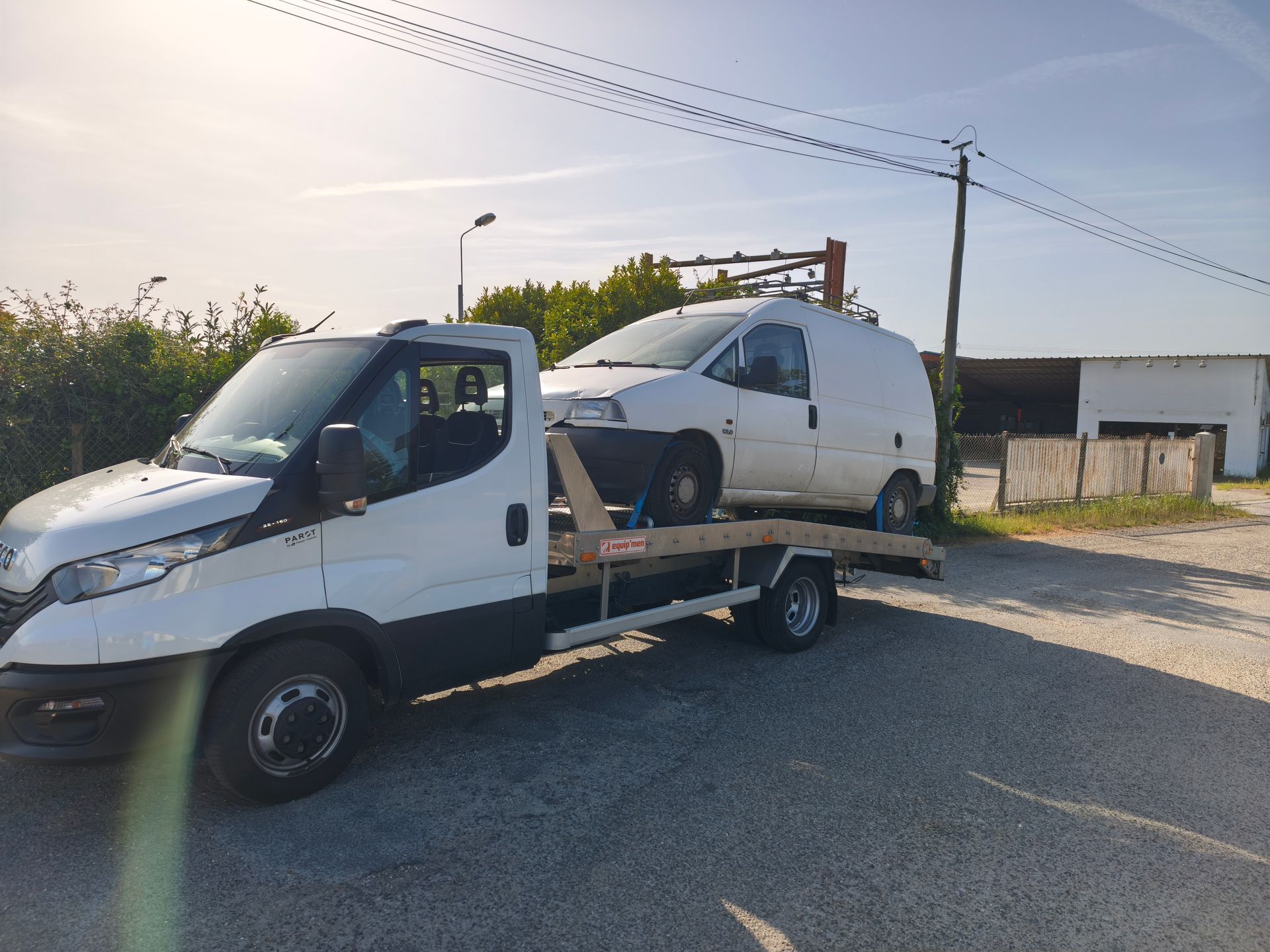 Une dépanneuse blanche transportant une camionnette blanche en bord de route, sous un soleil éclatant.