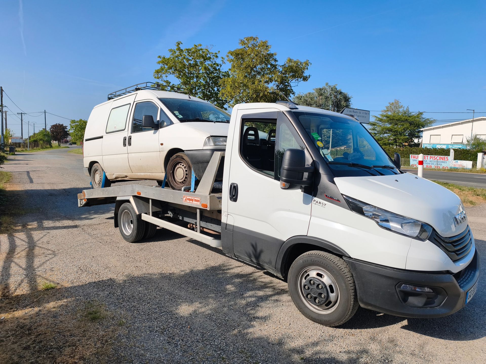 Un véhicule blanc se fait transporter par un petit camion.