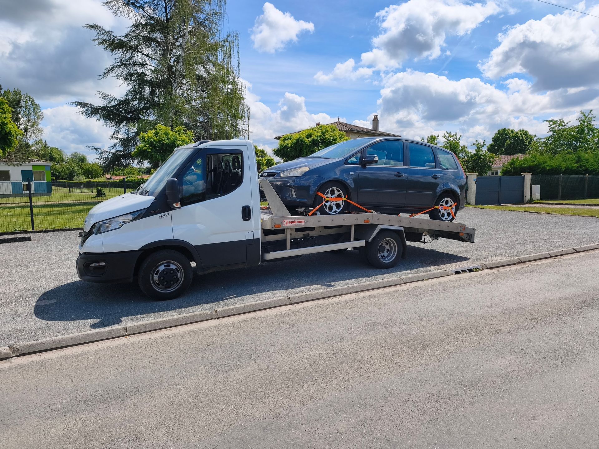 Une dépanneuse blanche transportant une voiture noire sur le bord de la route sous un ciel bleu nuageux.