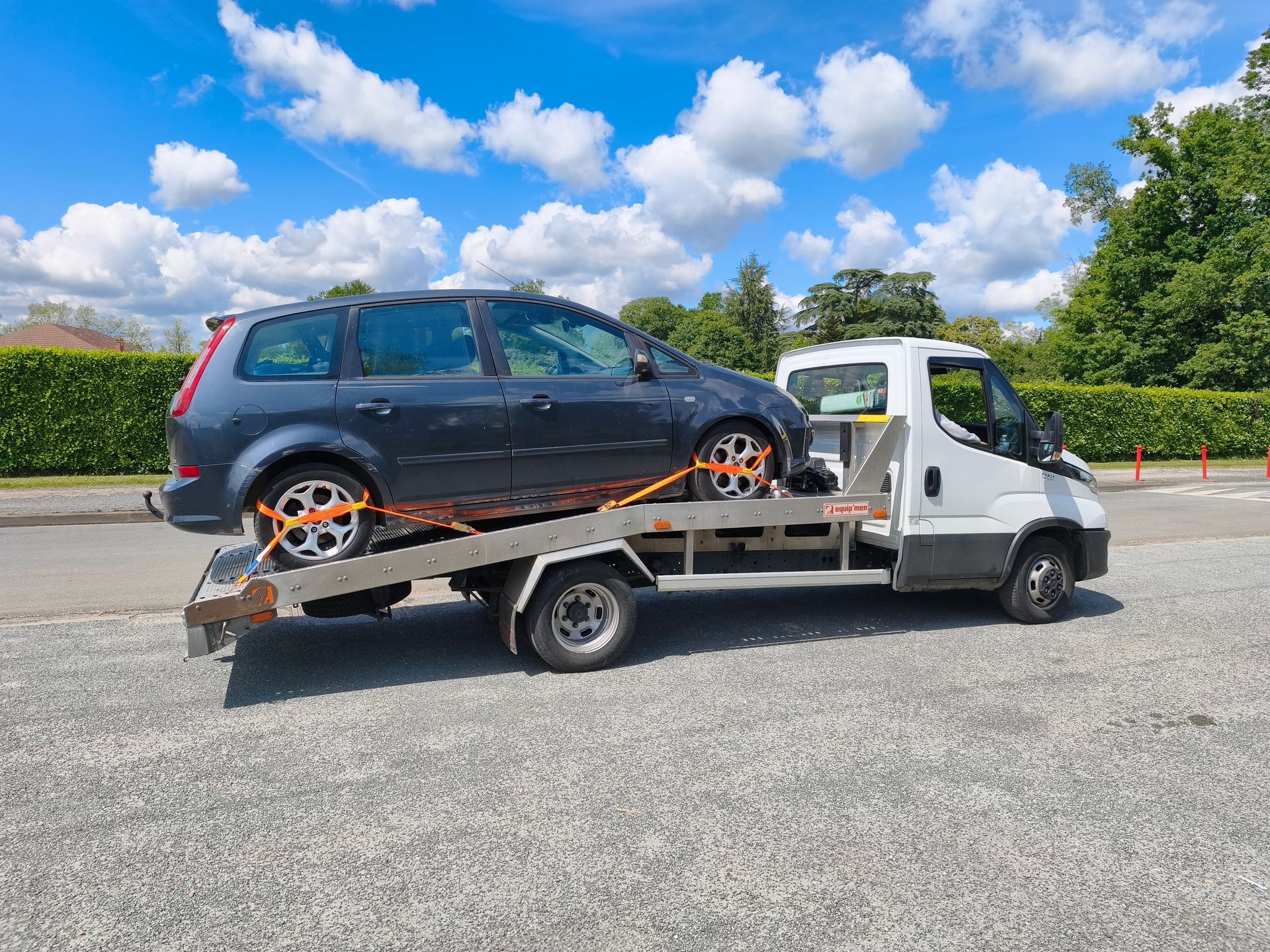 Une voiture sur une dépanneuse blanche, sur un terrain gravillonné sous un ciel nuageux et lumineux.
