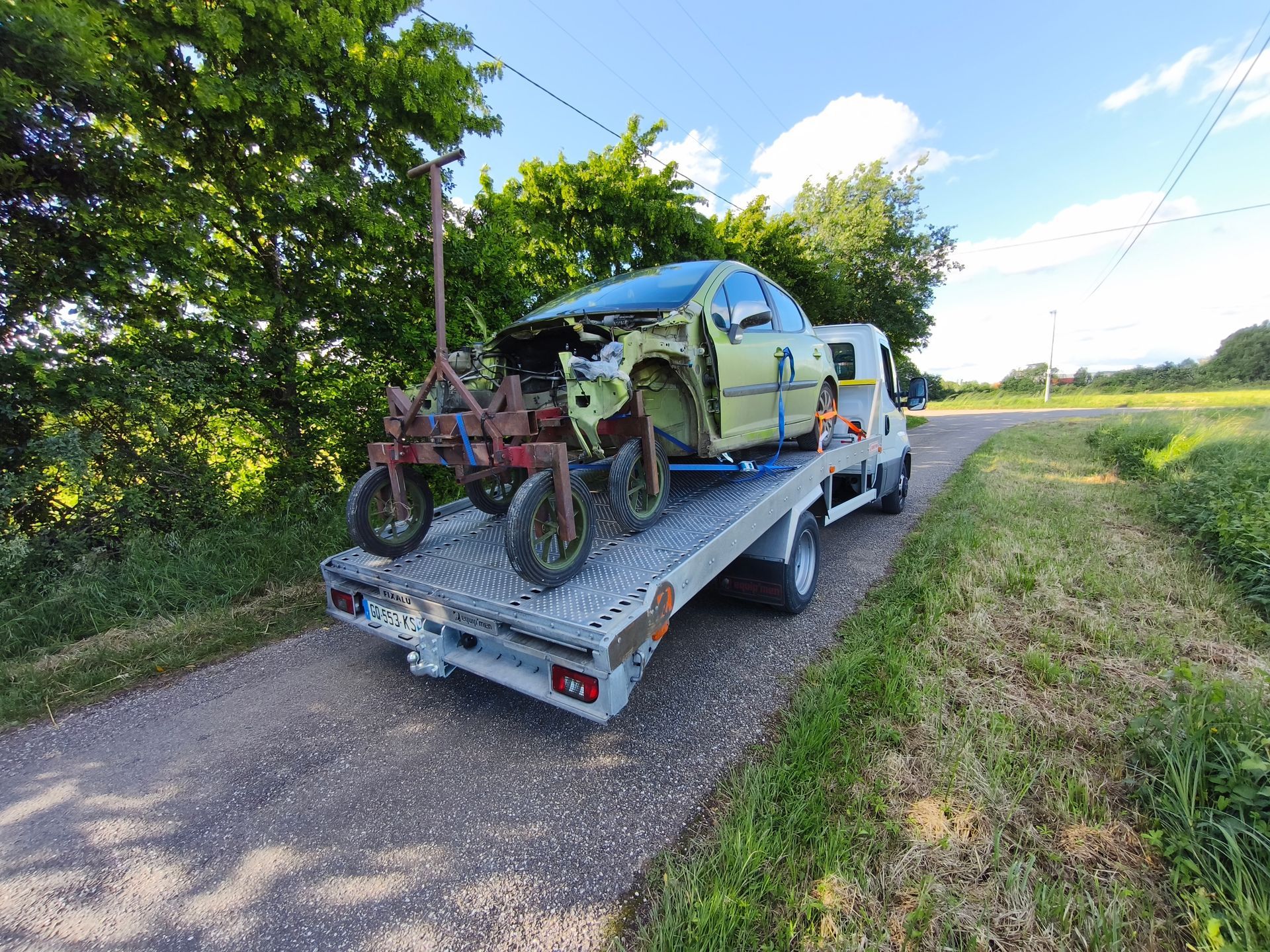 Une voiture verte emboutie et un outil agricole sur une dépanneuse.