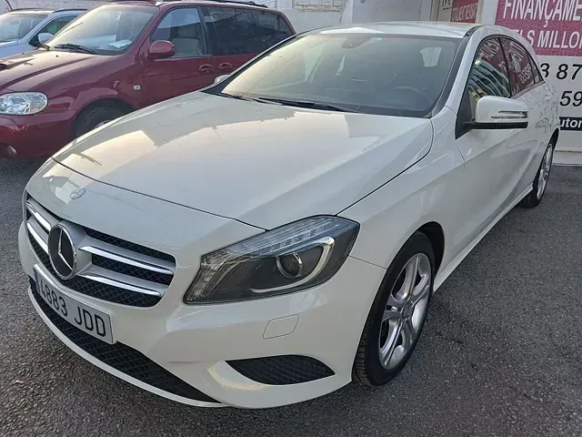 Un Mercedes Benz Clase A de color blanco está estacionado frente a un concesionario de automóviles.