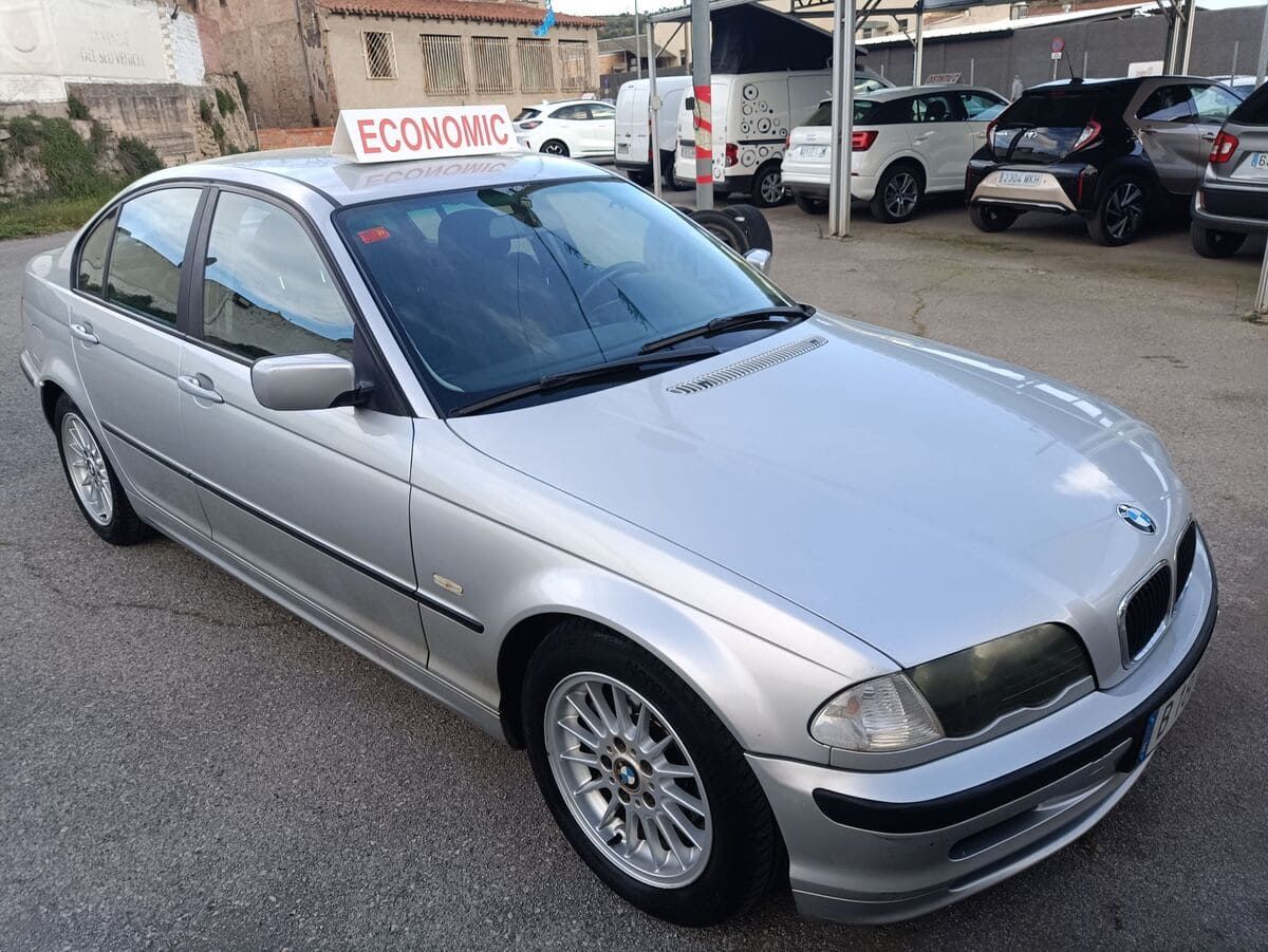 Un Suzuki Ignis gris estacionado en un aparcamiento pavimentado, con llantas de aleación negras y barras en el techo, con un telón de fondo de edificios.