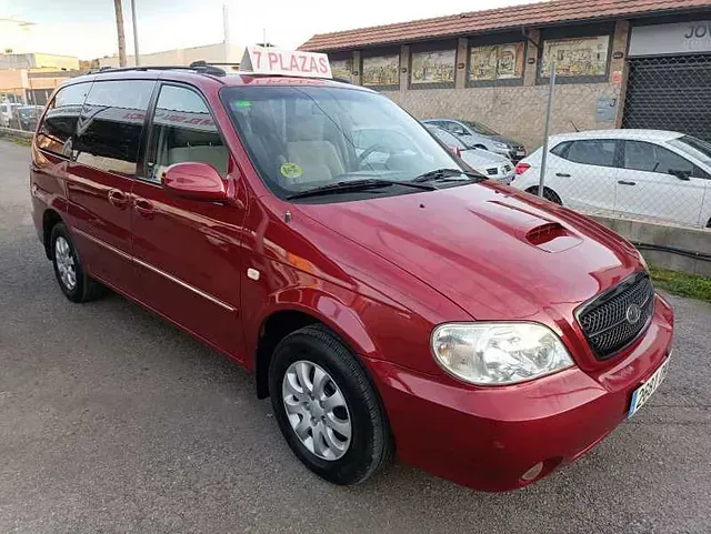 Una minivan roja está estacionada al costado de la carretera frente a un edificio.