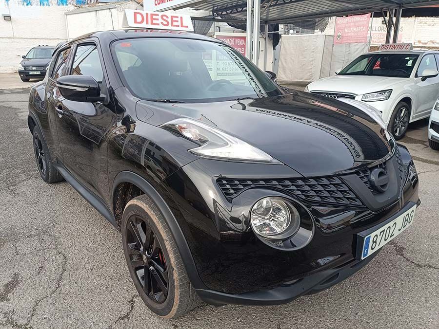 Nissan Juke negro estacionado al aire libre con un cartel "DIESEL" en el fondo.