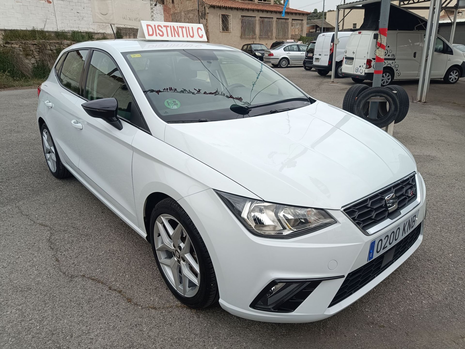 Un SEAT Ibiza blanco aparcado al aire libre con un letrero de "DISTRITO C" en el techo.