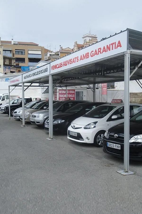 Estacionamiento de un concesionario de automóviles con autos estacionados bajo una marquesina y una pancarta roja con la palabra