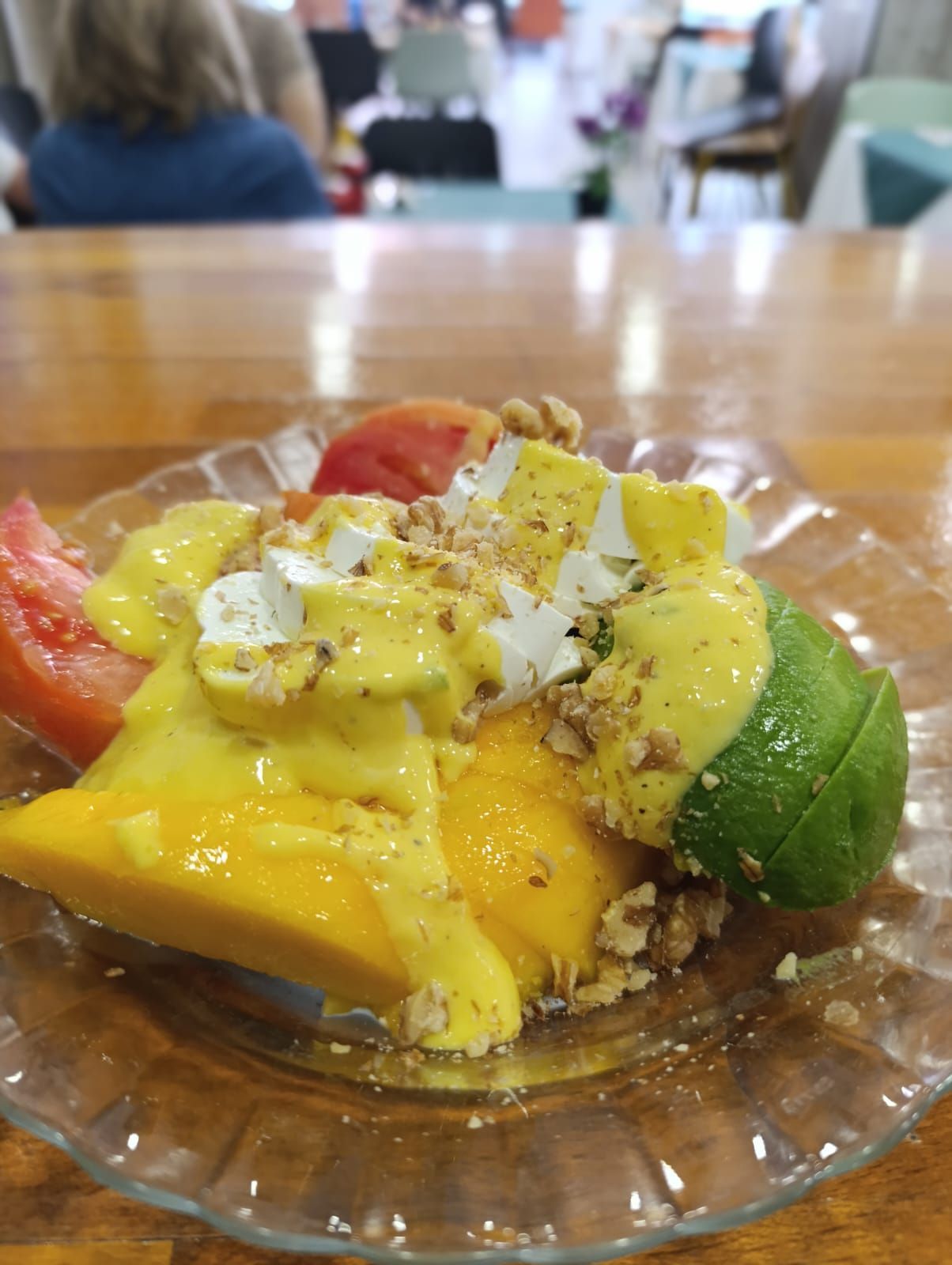 Ensalada de mango y aguacate con aderezo, nueces y tomate en plato de vidrio.