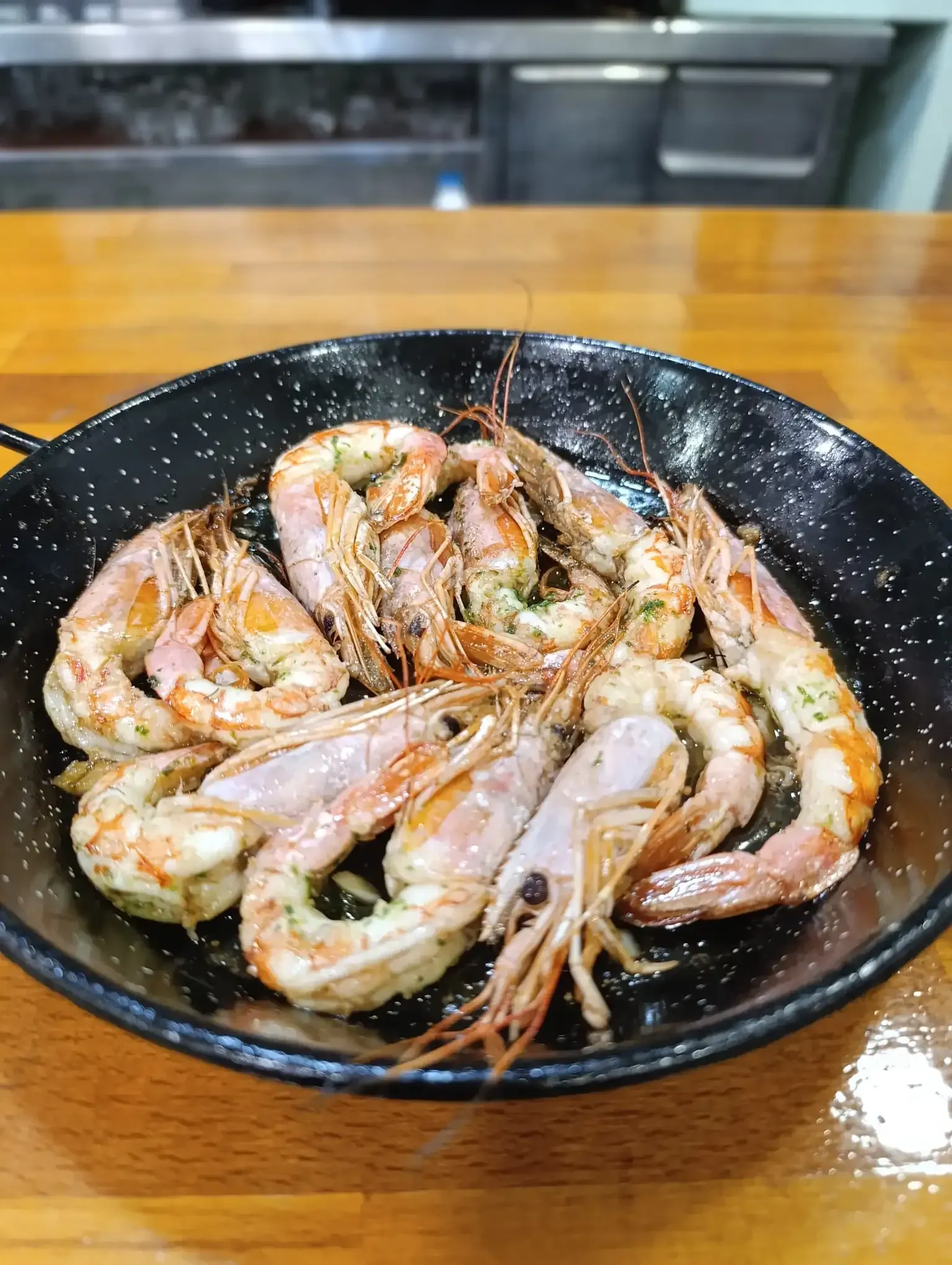 Camarones a la parrilla en una sartén negra sobre una mesa de madera.