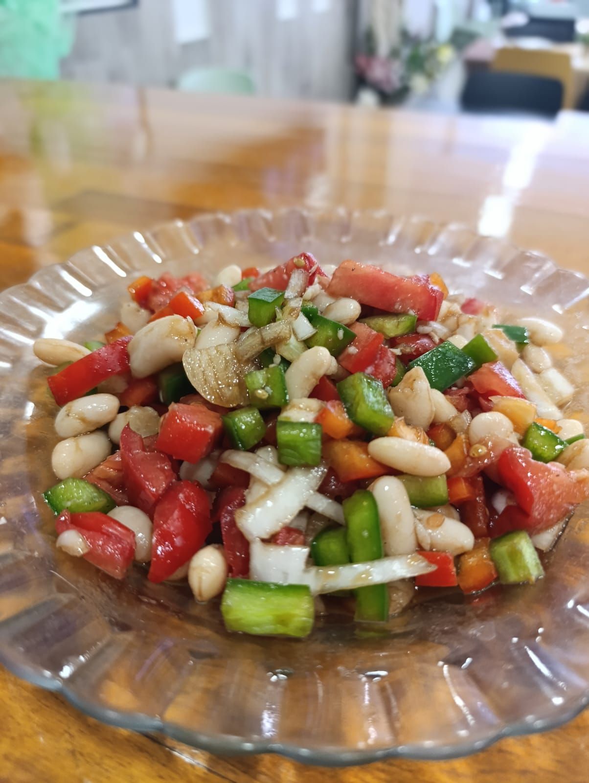 Ensalada con tomates, frijoles, pimientos y cebollas en un recipiente de vidrio transparente sobre una mesa de madera.