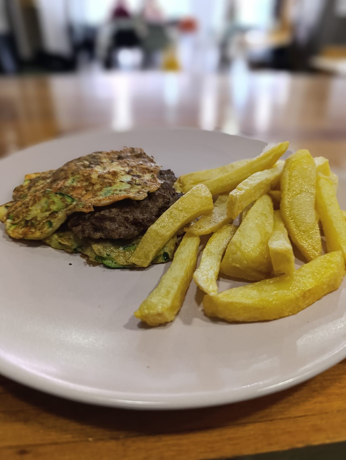 Hamburguesa sobre buñuelo de calabacín, con patatas fritas en un plato.