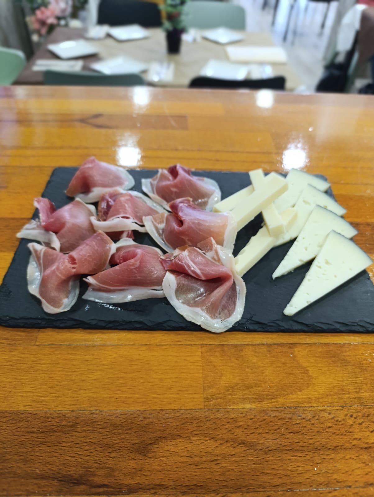 Jamón y queso en lonchas sobre una bandeja de pizarra negra encima de una mesa de madera.