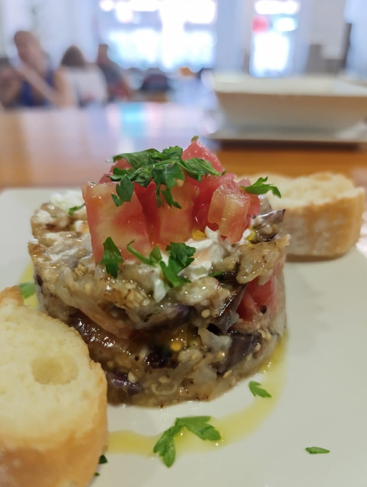 Pila de aperitivo de berenjena, tomate y queso, adornado con perejil, servido con pan.