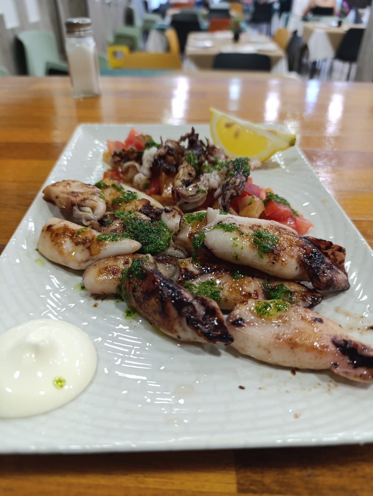 Plato de calamares a la plancha con ensalada de tomate, rodaja de limón y salsa en un plato rectangular blanco.