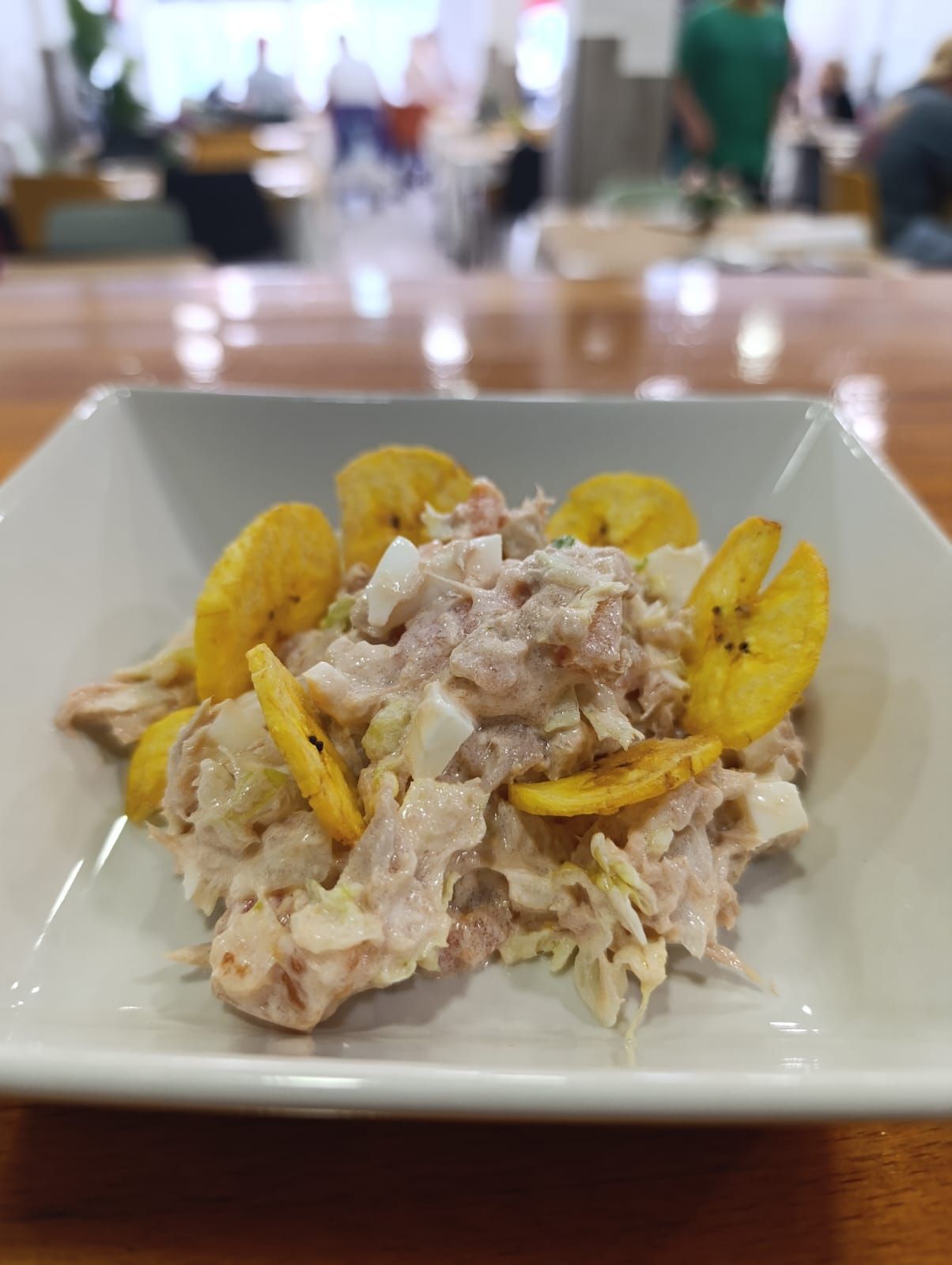 Tazón blanco de ensalada de atún con plátanos fritos, sobre una mesa de madera.