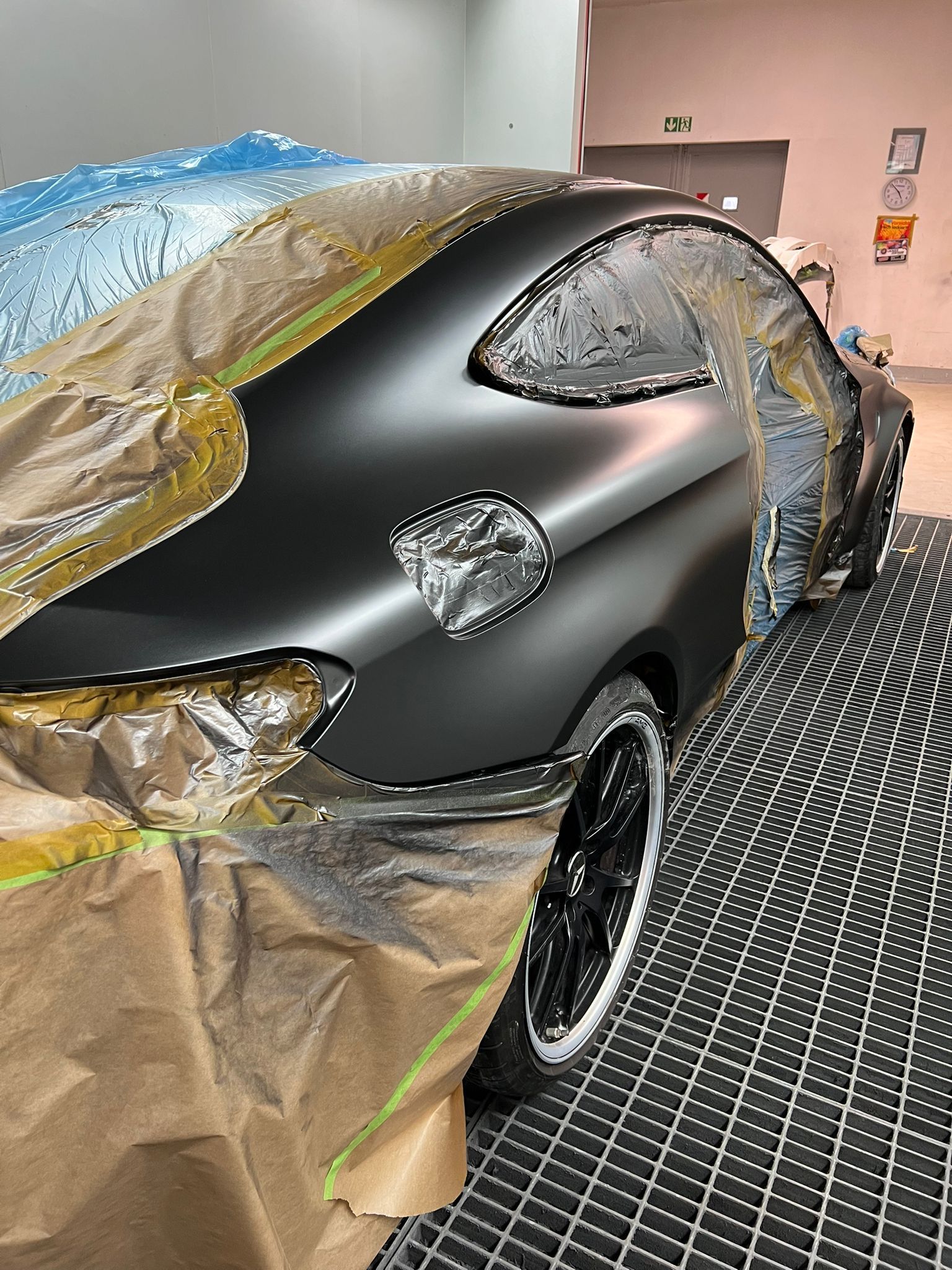 Nahaufnahme eines schwarzen Autos in der Lackierkabine, dessen obere Hälfte für Lackierarbeiten abgeklebt ist.