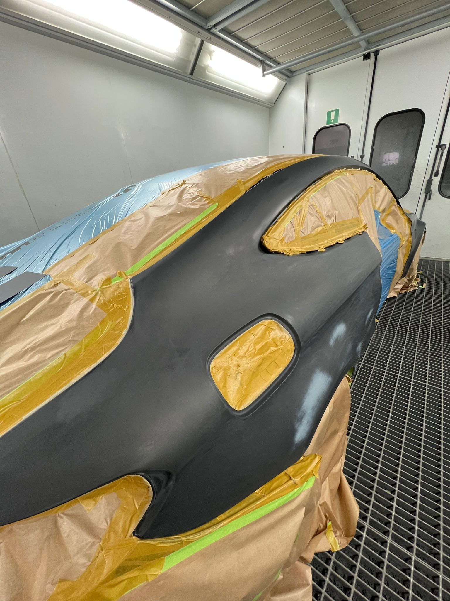Abgeklebtes schwarzes Auto in der Lackierkabine; Dach und Scheiben mit blauer Folie und braunem Papier geschützt.