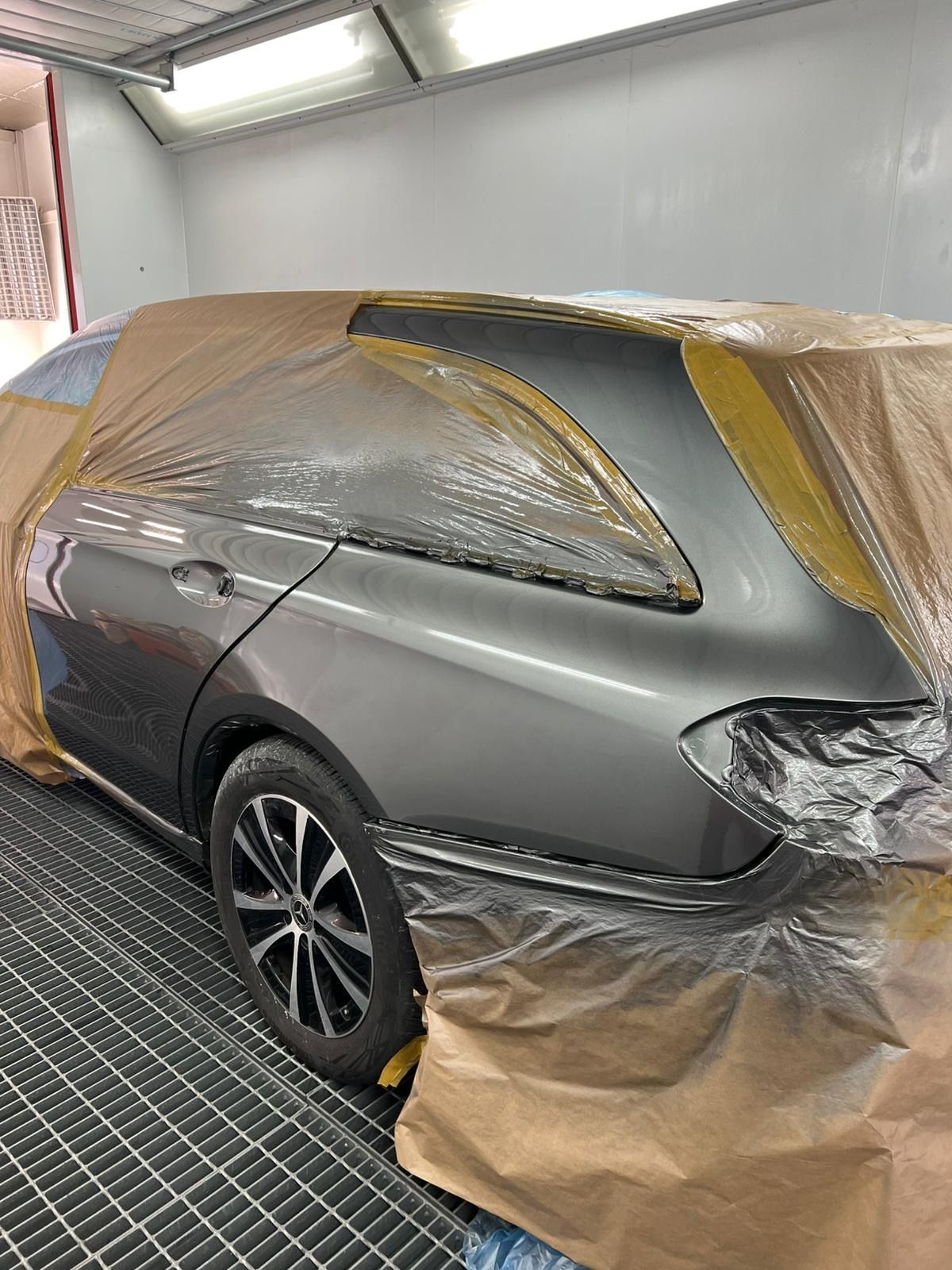 Heckbereich eines hellgrauen Autos in der Lackierkabine, großflächig mit braunem Papier zum Schutz abgeklebt.