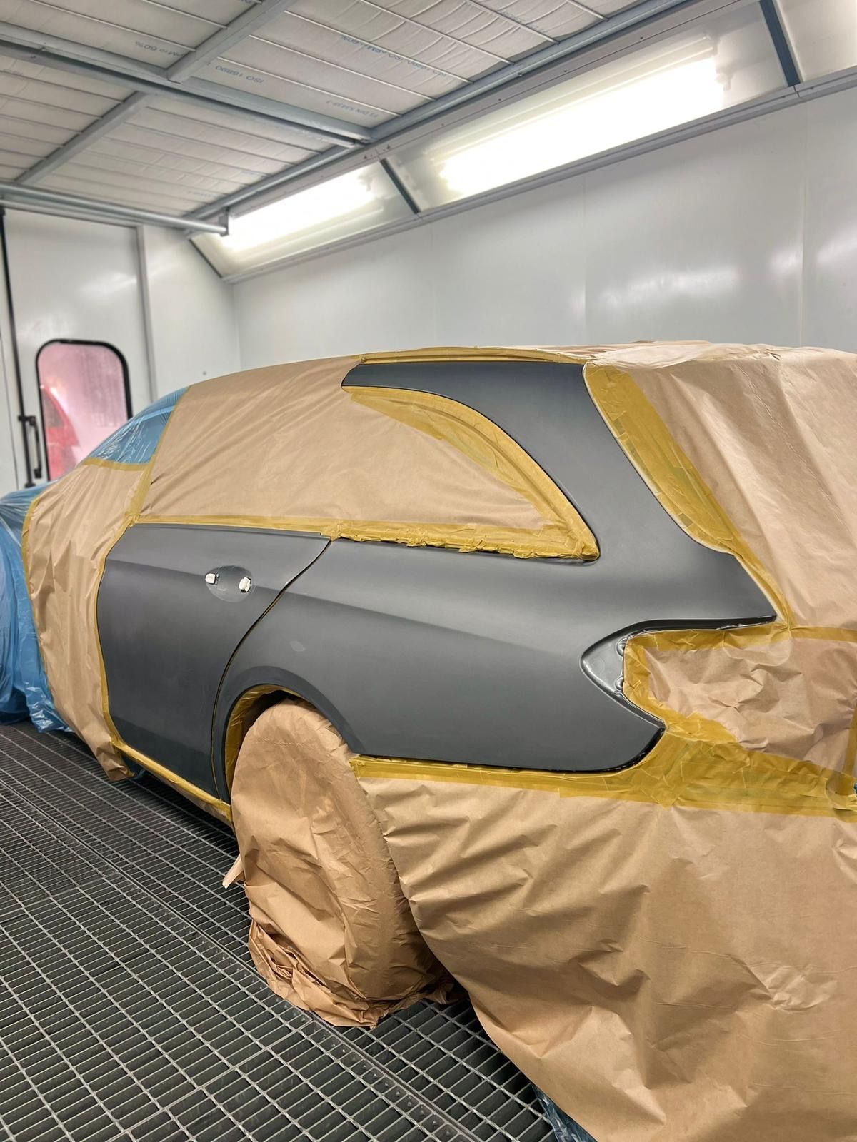 Frontpartie und Dach eines hellgrauen Autos in der Lackierkabine, teilweise mit Papier und Folie abgeklebt.