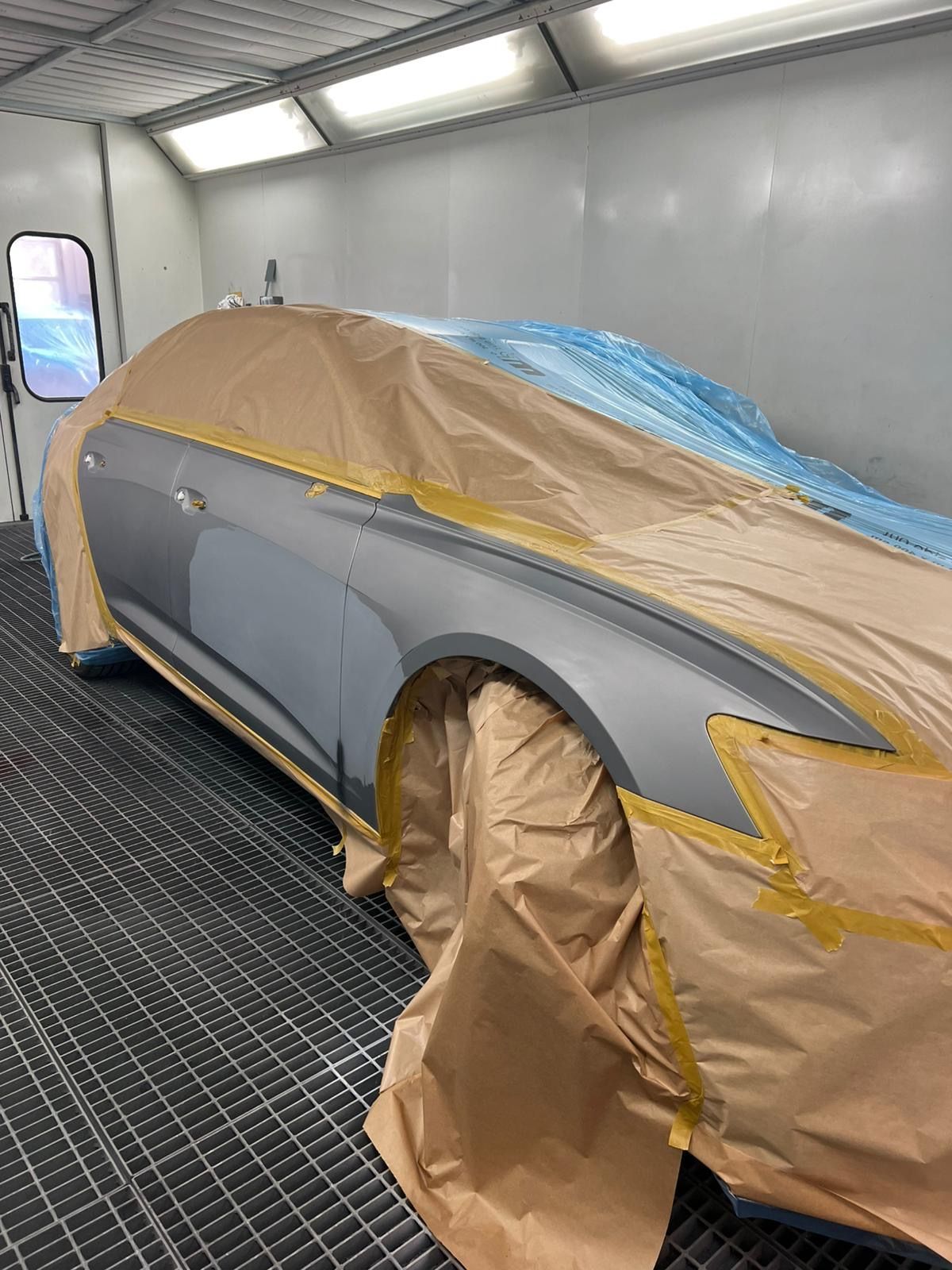 Hellgraues Auto in der Lackierkabine, Oberseite komplett mit braunem Papier und blauer Folie maskiert.