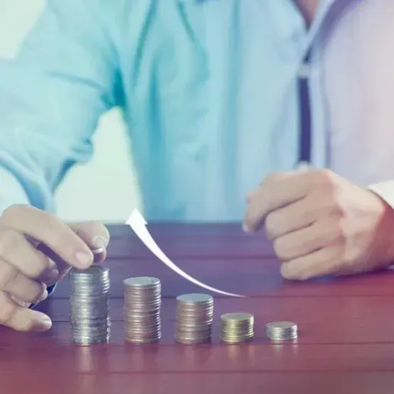 Un hombre está sentado en una mesa con pilas de monedas y un gráfico que va subiendo.