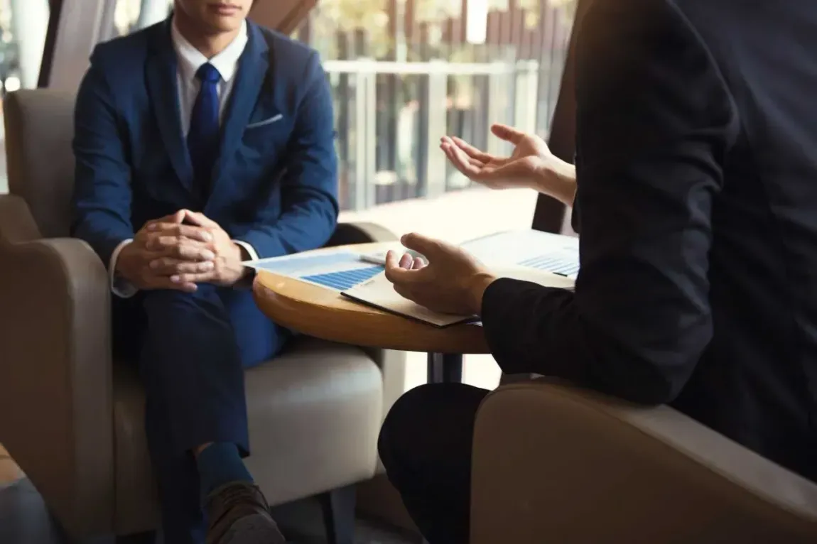 Dos hombres de traje están sentados en una mesa conversando.