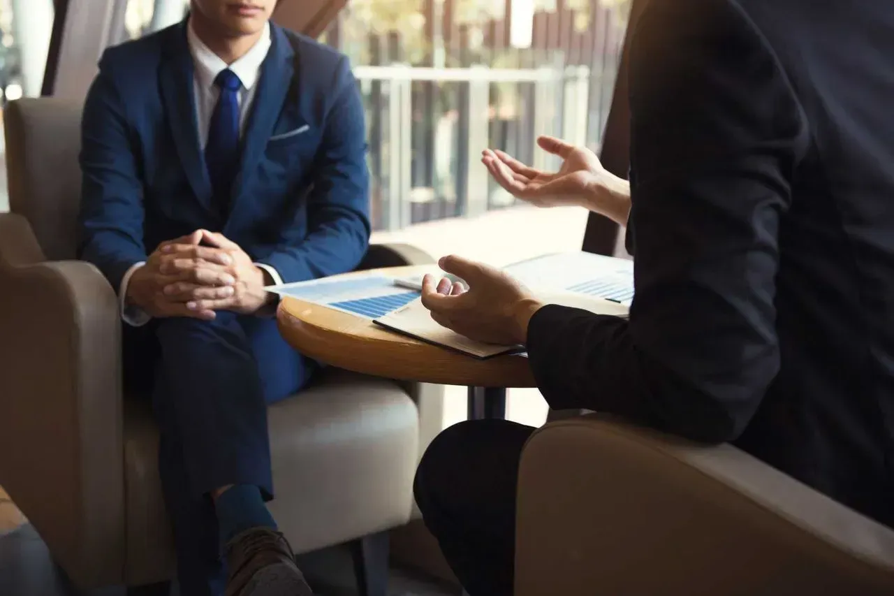 Dos hombres de traje están sentados en una mesa conversando.