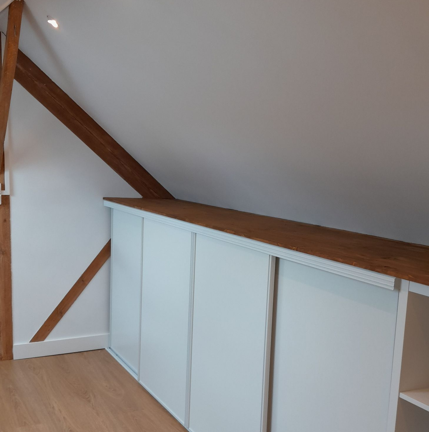 Armoires de rangement blanches encastrées dans un mur en angle, sous une poutre en bois.