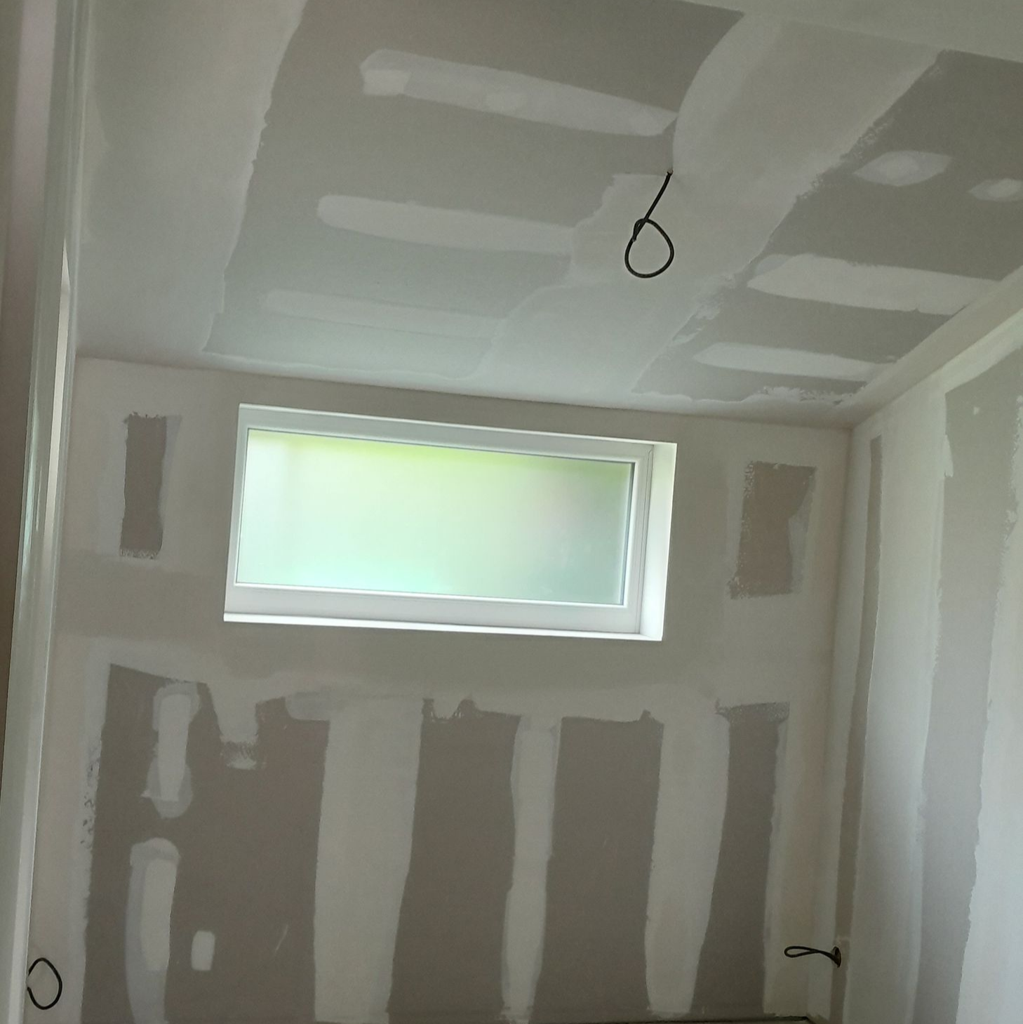 Pièce intérieure en cours d'aménagement, avec des plaques de plâtre installées aux murs et au plafond, une fenêtre au centre.