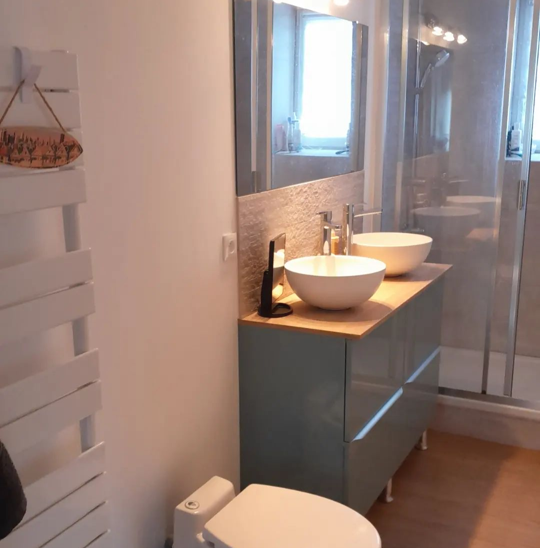 Salle de bains avec meuble-lavabo bleu, lavabos blancs, miroir et douche avec portes en verre.