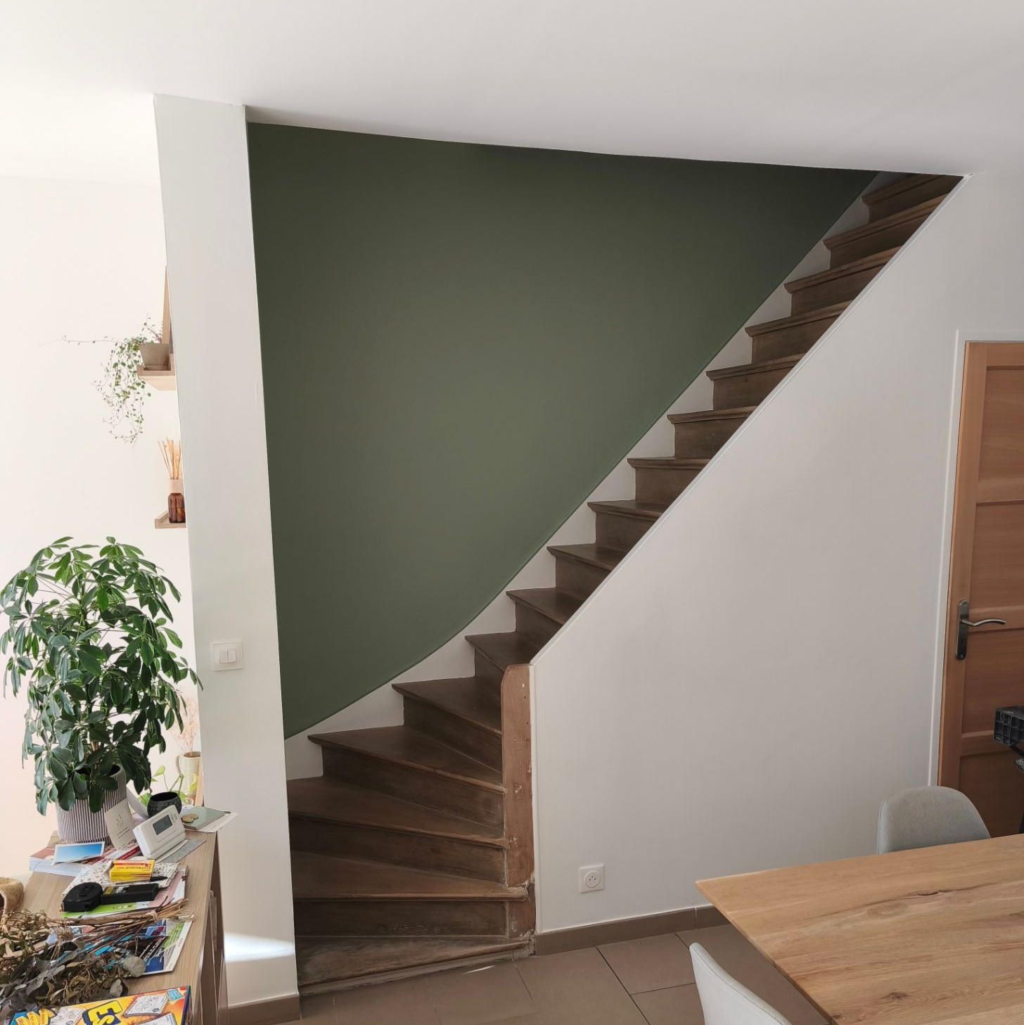 Escalier en bois devant un mur vert, murs blancs, intérieur.