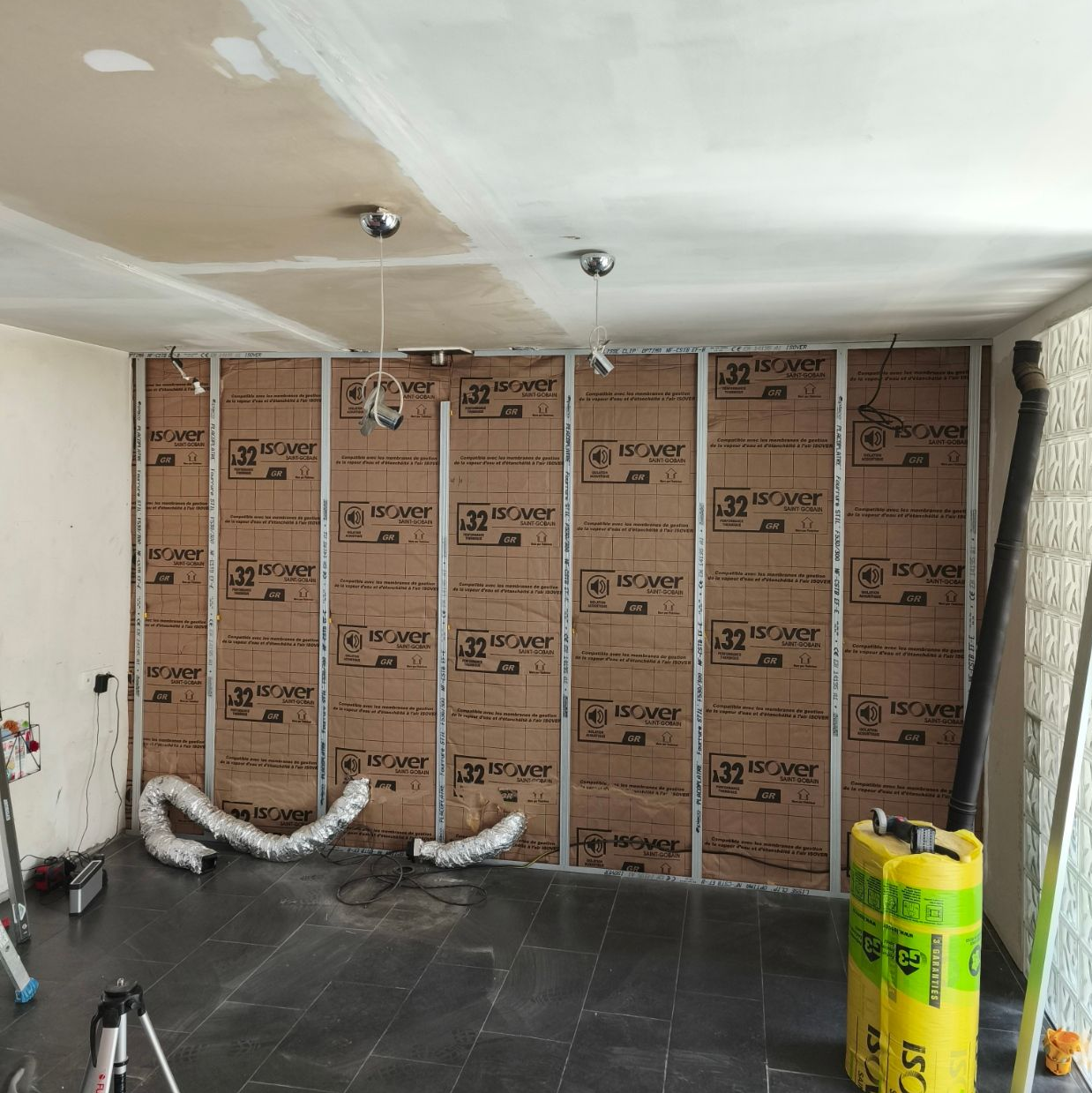 Mur intérieur en construction avec isolation entre les montants métalliques, plafond non fini et sol foncé.