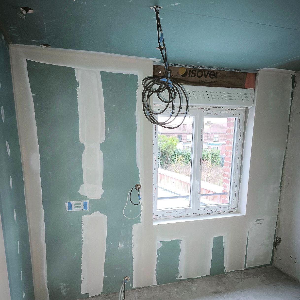 Pièce intérieure en cours d'aménagement, avec cloisons sèches et câblage. Une fenêtre est visible.