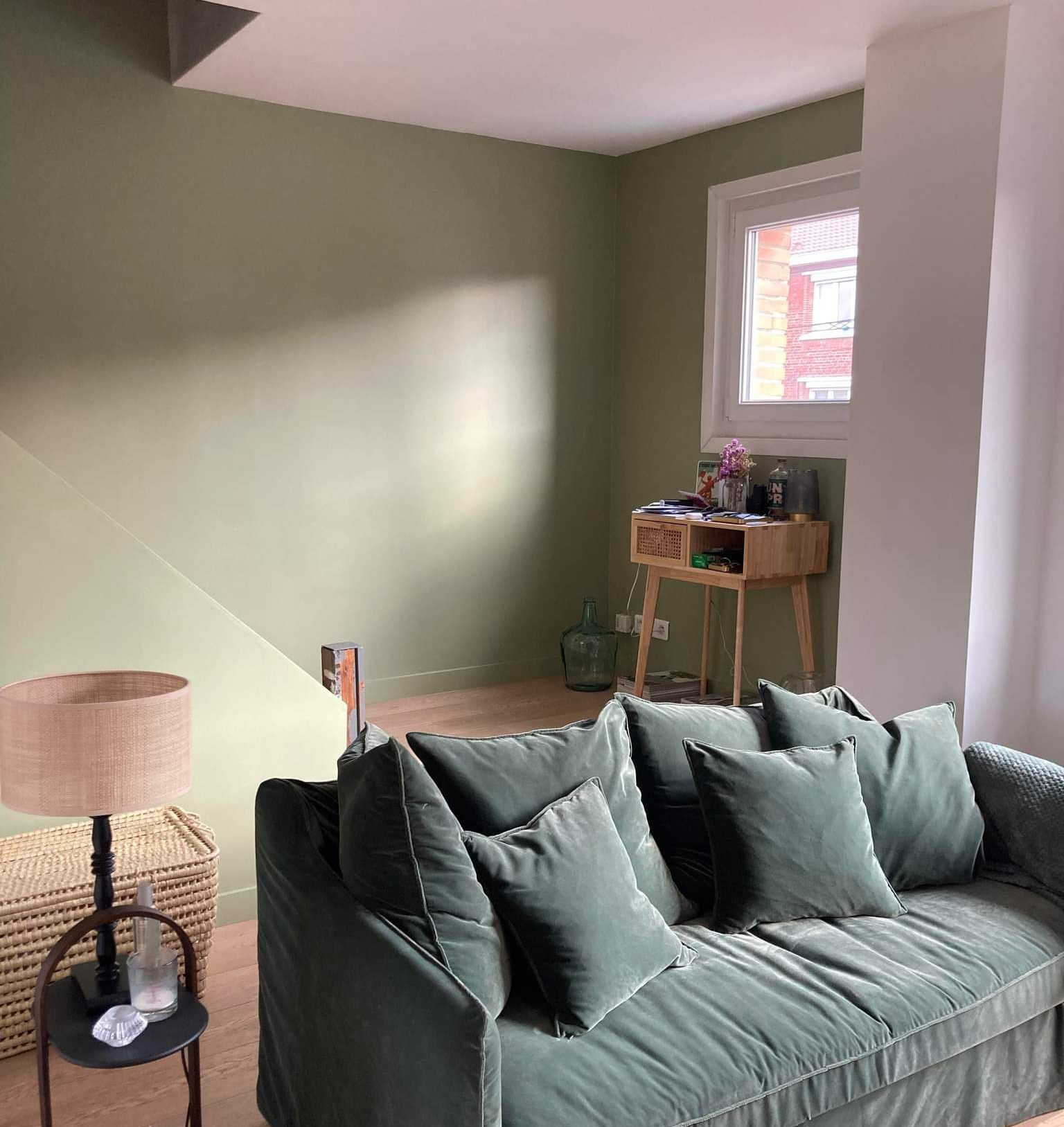 Salon peint en vert avec un canapé en velours vert, une petite table d'appoint et un lampadaire.