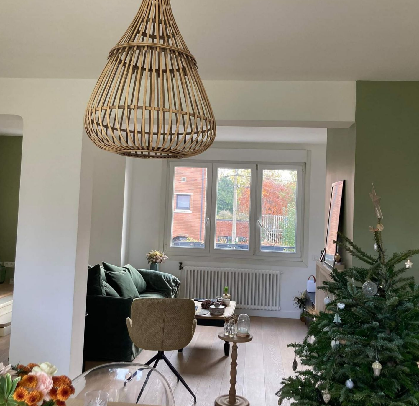 Salon avec sapin de Noël, murs verts et suspension lumineuse en tissu tressé.