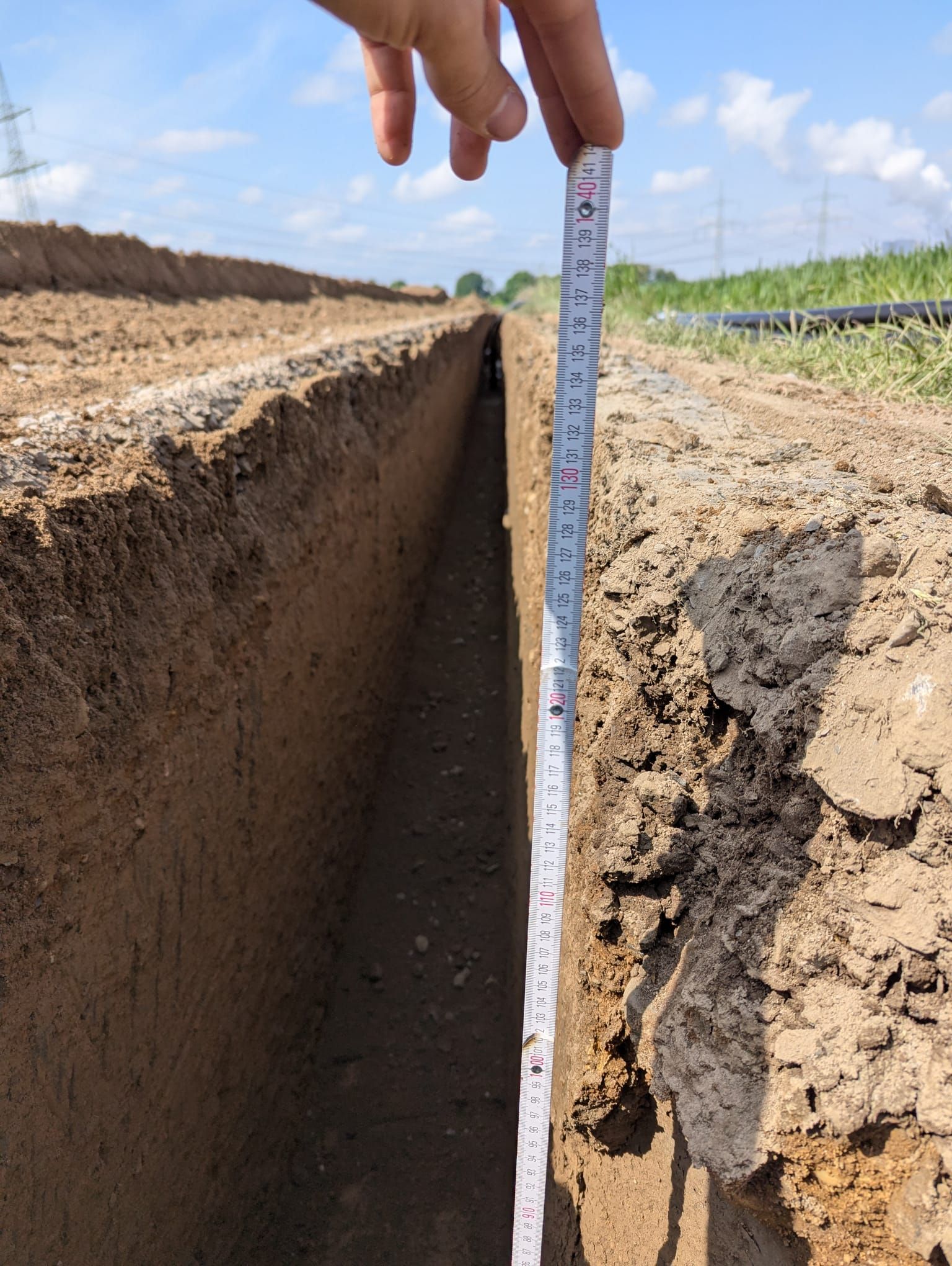 Eine Person, die mit einem Maßband die Tiefe eines Grabens misst