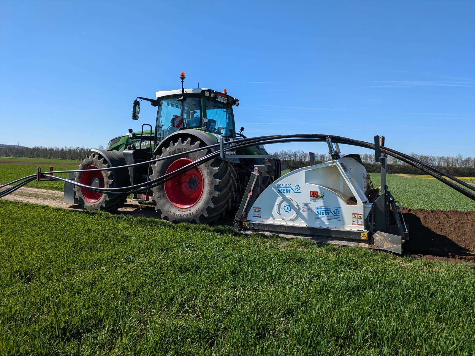 Ein Traktor pflügt ein Grasfeld mit einer daran befestigten Maschine