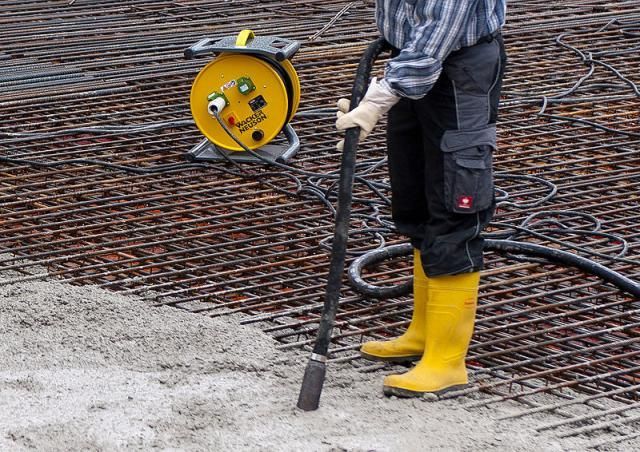 Ein Mann in gelben Stiefeln saugt eine Betonoberfläche mit einem Staubsauger.