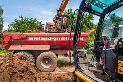 Ein Muldenkipper wird von einem Bagger mit Erde beladen.